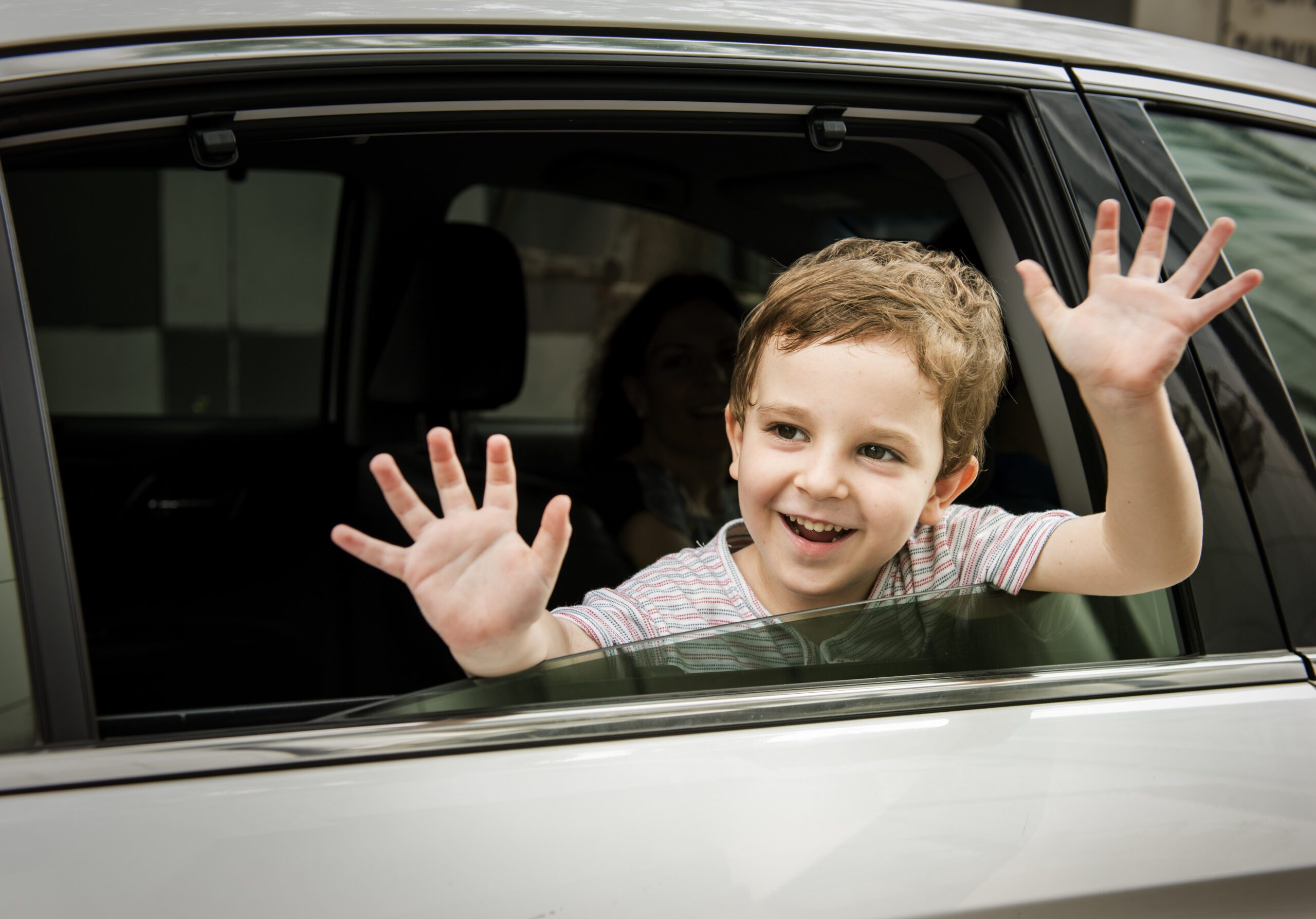 Smiling boy waving through a car window, looking cheerful and excited.